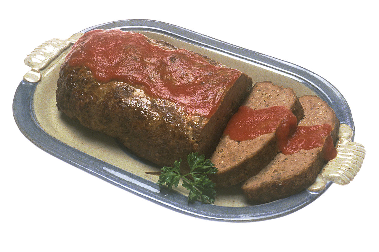 A classic meatloaf with tomato glaze on a serving platter with sliced pieces.