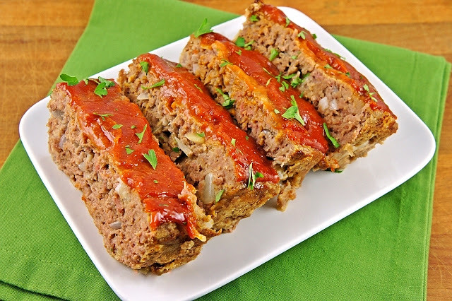 Thick slices of glazed meatloaf arranged on a white platter over a green napkin.